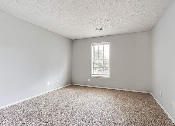 A room with a carpeted floor and a window with blinds.