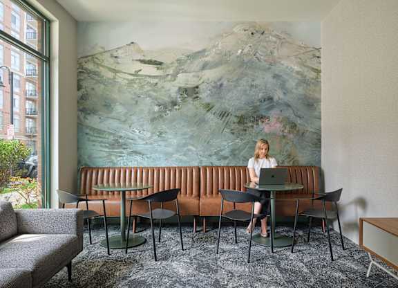 A woman is sitting at a table in front of a large painting.