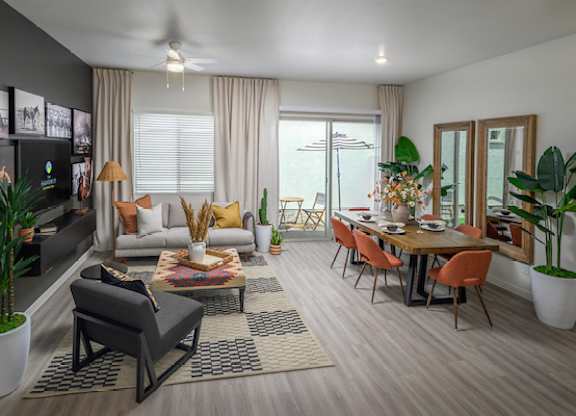 A modern living room with a grey sofa, a wooden dining table, and a ceiling fan.