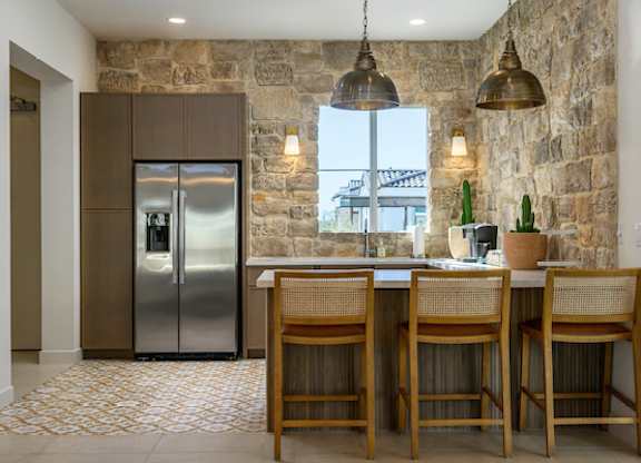 A kitchen with a stone wall and a stainless steel refrigerator.
