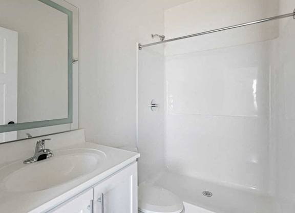 A white bathroom with a sink, toilet, and shower.