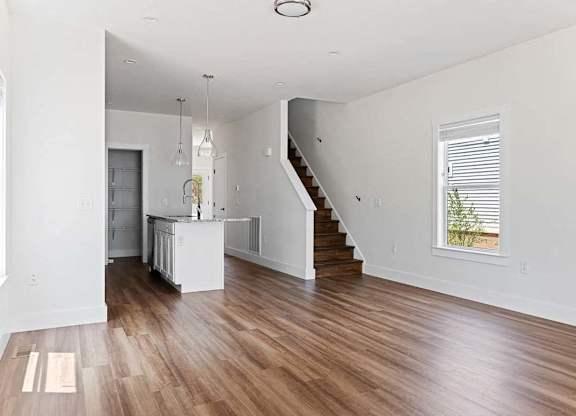 A large open living space with wood flooring and a staircase leading to the upper level.