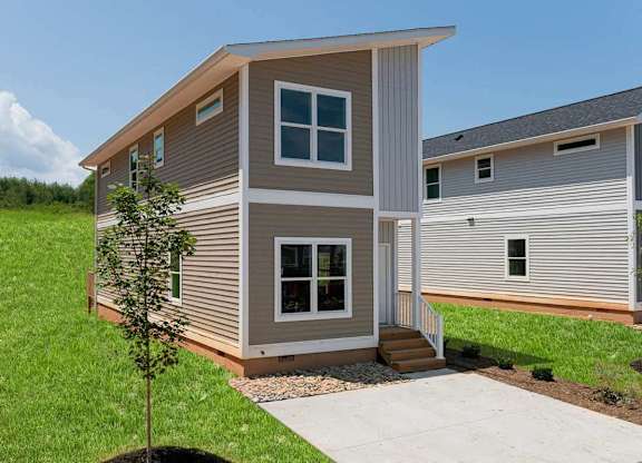 A modern house with a grey and beige exterior and a small tree in front.