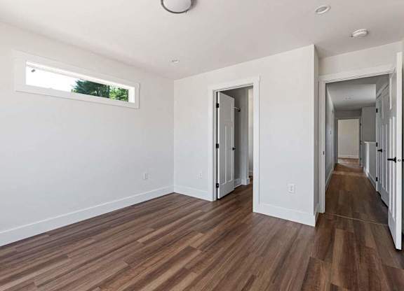 A room with white walls and wooden flooring with a window.