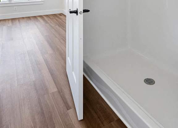 A white door is open to a bathroom with a white tub and a wooden floor.