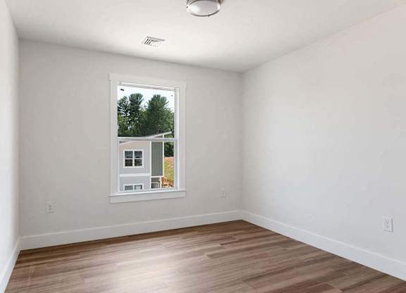 A room with a window showing a view of trees and a house.