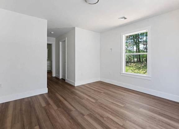 A room with wooden floors and a window showing trees outside.