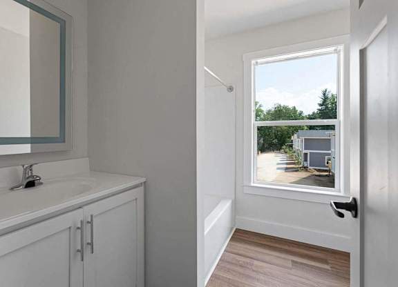 A bathroom with a white sink and a window with a view of a house.