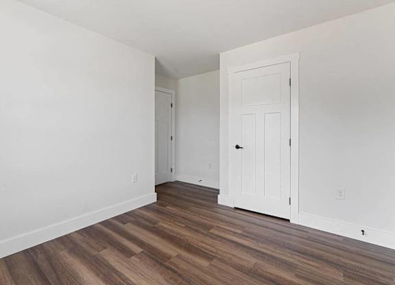 A room with white walls and wood flooring with a door on the right.