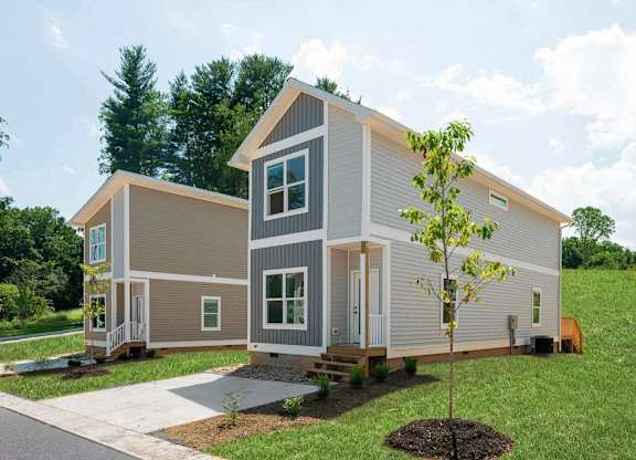 A modern house with a grey and white exterior and a small tree in front.