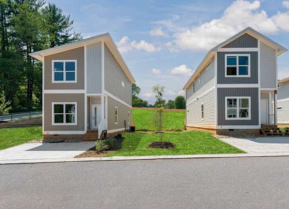 Two modern houses with grey and brown siding are situated in a residential area.