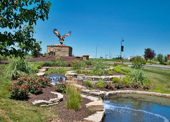 A statue of a bird is perched on a rock in a garden.