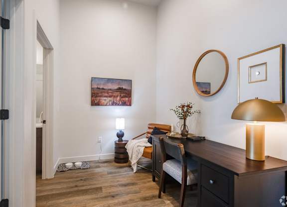 A room with a painting on the wall and a lamp on the desk.