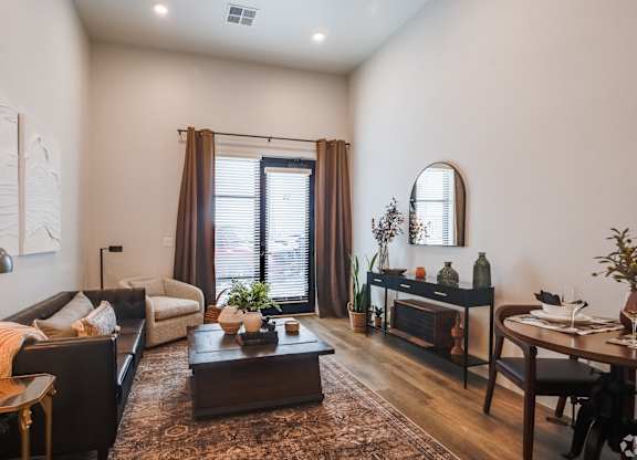 High-end Apartments in Greeley CO - The Shelby - Spacious Living Room with a Brown Coffee Table, Sofa, Armchair, Dining Table, and Large Window