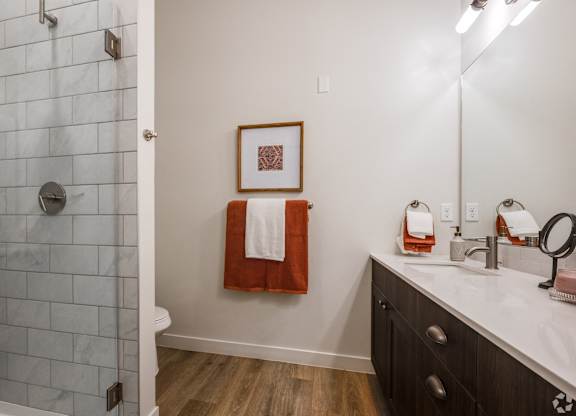 A bathroom with a white tiled shower and a white sink with a red towel hanging on the wall.