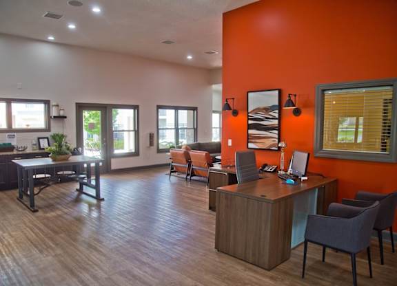 A room with orange walls and wooden floors has a desk and chairs in it.