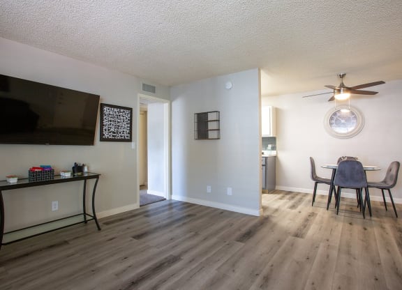 Tucson, AZ, Apartments - Peaks at Redington - Open Floor Plan Living Room with Wood-Style Flooring, TV, and View of Dining Area and Kitchen.
