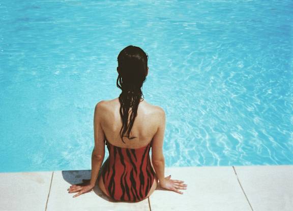 A woman in a striped swimsuit sits by a pool.