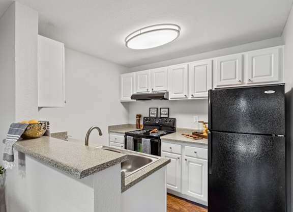 A black refrigerator is in the corner of a white kitchen at MonteVista Apartments, Beaverton