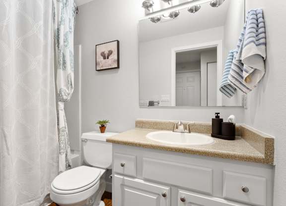 A white bathroom with a toilet, sink, and mirror at MonteVista Apartments, Oregon 97007
