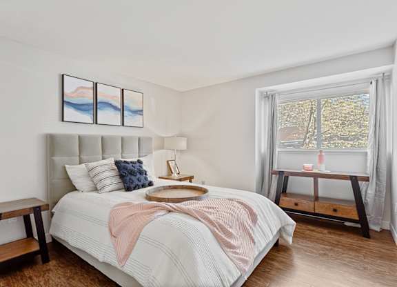 A bedroom with a large bed and a window overlooking a tree-lined street at MonteVista Apartments, Beaverton, Oregon