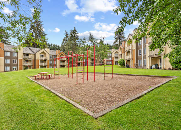 A playground with a red swing set in the middle of a grassy area at MonteVista Apartments, Beaverton, OR
