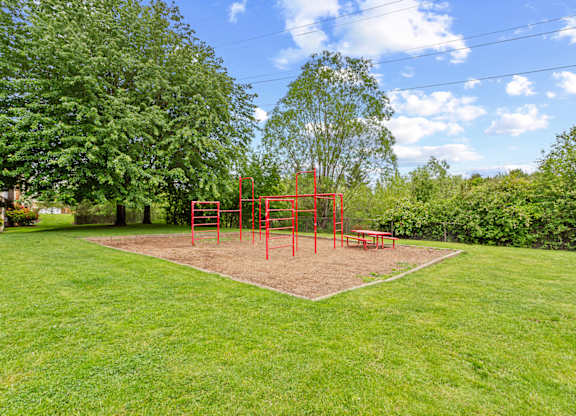 A playground with a red swing set in the middle of a grassy area at MonteVista Apartments, Beaverton, 97007