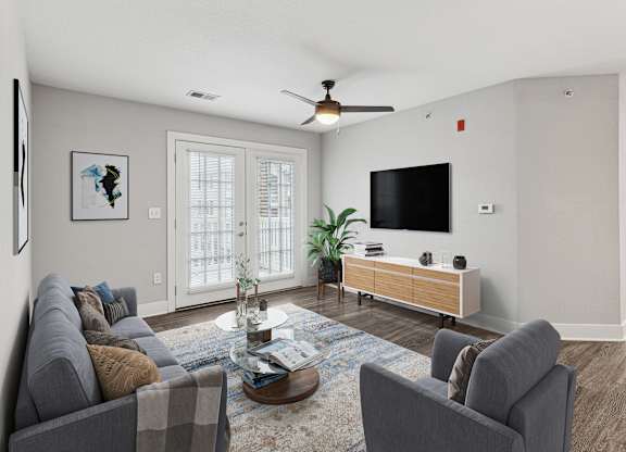 A living room with a grey couch, a coffee table, and a flat screen TV mounted on the wall.