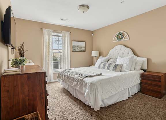 One, Two and Three- Bedroom Apartments for Rent in Sevierville, TN – Overlook at Allensville – A bedroom with a large bed, a dresser, and a window with curtains.