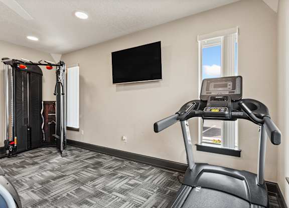 A treadmill is in a room with a television mounted on the wall.