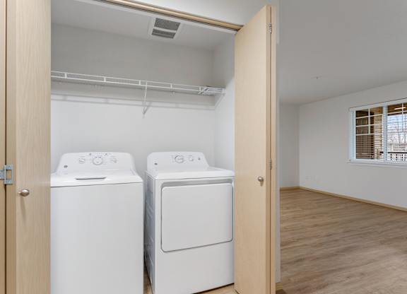 Apartments for Rent in Vancouver, WA - Reflections at the Park - Laundry Closet with Washer and Dryer, Wood-Style Flooring, and Wire Rack Shelf.