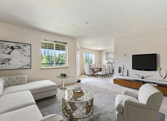One Bedroom Apartments in Vancouver, WA - Reflections at the Park - Living Room with Carpeting, Sectional Couch, TV, and View of Dining Area.
