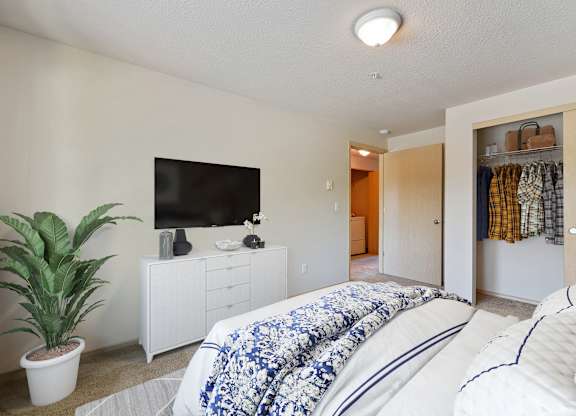 Apartments for Rent in Vancouver, WA - Reflections at the Park - Spacious Bedroom with Plush Carpet Flooring, Bed, Dresser, TV, Housplant, and Sliding Door Closet