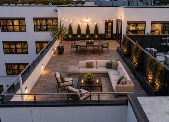 A rooftop patio with a couch, chairs, and string lights.