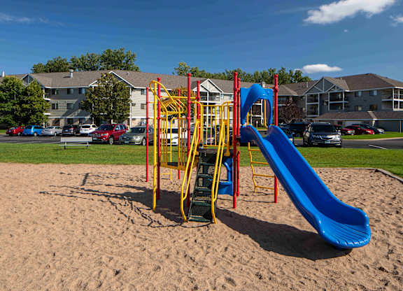 A playground with a blue slide and yellow and red climbing structure.