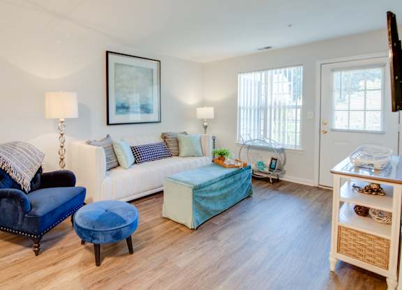 A living room with a blue chair and ottoman, a white couch, and a television on a stand.