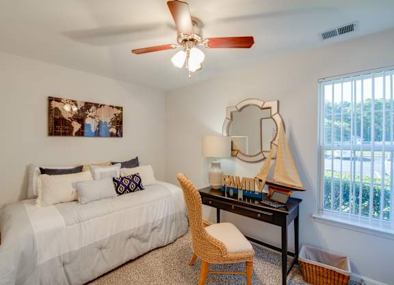 A bedroom with a bed, desk, chair, and a window.