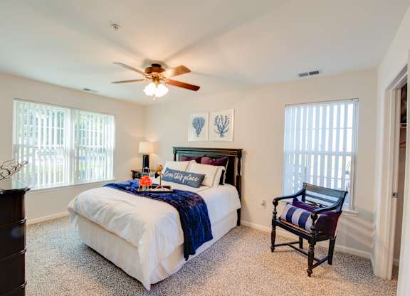 A bedroom with a bed, chair, and ceiling fan.