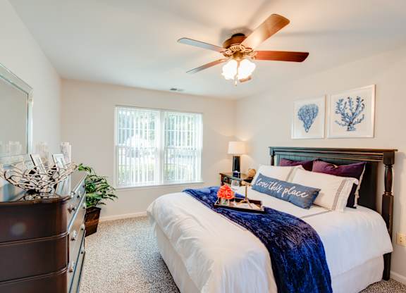 A bedroom with a bed, a dresser, a ceiling fan, and a window.