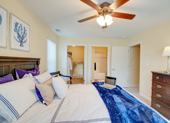 A bedroom with a bed, a ceiling fan, and a laptop on the bed.
