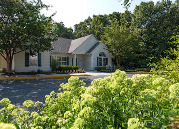 A white house with a grey roof is surrounded by greenery.