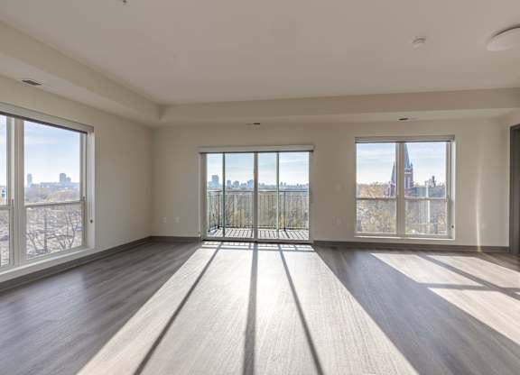 A spacious room with wooden floors and large windows overlooking a cityscape.