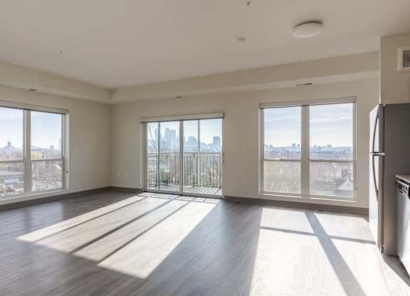 A large, empty room with wooden floors and a view of the city through large windows.