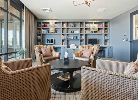 A living room with a black coffee table surrounded by brown patterned chairs and a bookshelf filled with books.