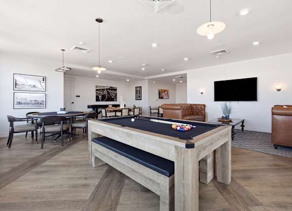 A pool table is in the middle of a room with a leather couch and a TV mounted on the wall.