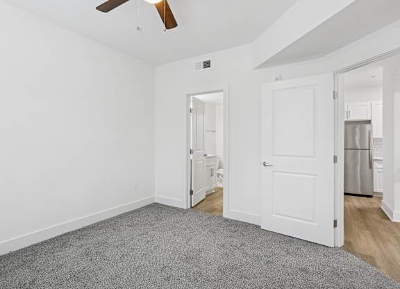 A room with a ceiling fan and a door leading to a kitchen.