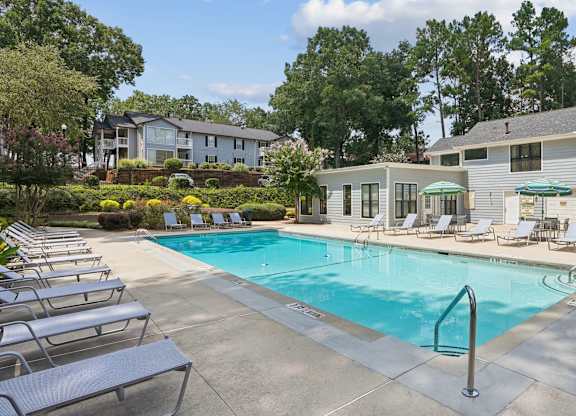 A swimming pool surrounded by lounge chairs and trees.