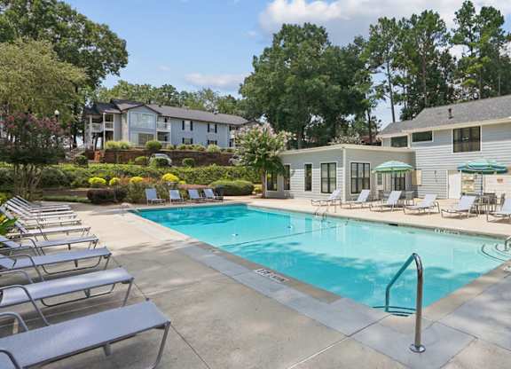 A swimming pool surrounded by lounge chairs and trees.