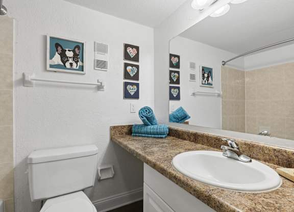 A bathroom with a toilet, sink, and pictures on the wall.