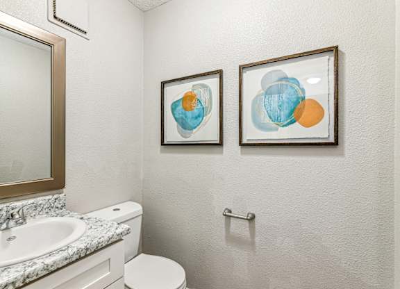 A bathroom with a toilet, sink, and two framed artworks on the wall.
